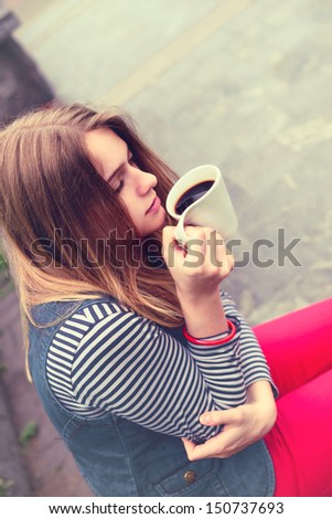 beautiful girl during a rain under umbrella drinks hot coffee outdoor
