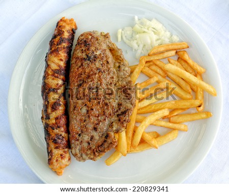 Grilled stuffed sliced pork loin and stuffed burger with french fries and chopped onion served on white plate.