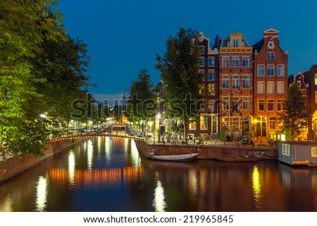 Night city view of Amsterdam canal, bridge and typical houses, boats and bicycles, Holland, Netherlands.