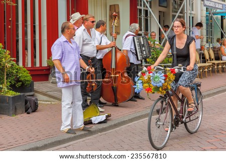 Amsterdam, Netherlands - July 29,2014: A typical Amsterdam street with cyclist and street musicians (Buskers) near cafes.  In Amsterdam, there are about 600,000 bikes. Focus on cyclists.