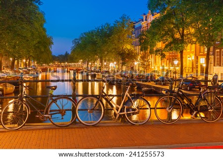 Night city view of Amsterdam canal, bridge, boats and bicycles, Holland, Netherlands.