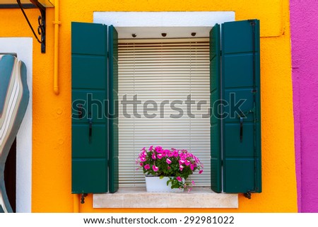 Picturesque window with shutters and flowers on orange wall of houses on the famous island Burano, Venice, Italy