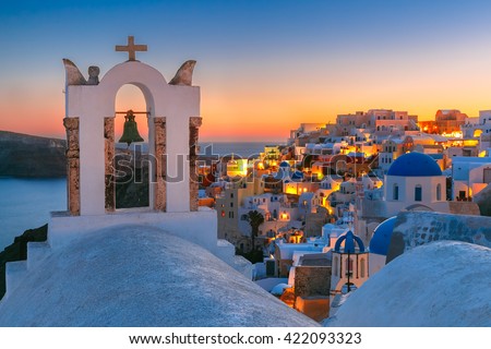 Arch with a bell, white houses and church with blue domes in Oia or Ia at sunset, island Santorini, Greece