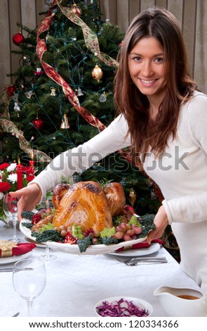 Family christmas dinner celebration. Woman holding Roasted turkey, red candles, fir tree ornament decoration, rich table with meals. Focus on turkey