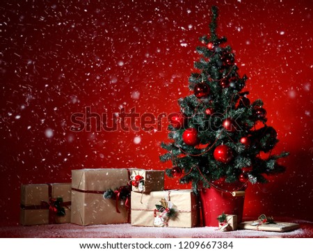 Christmas tree decorated with red patchwork ornament balls and craft presents gifts for new year 2019  under heavy snow on dark red background