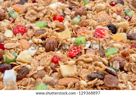 Muesli cereals background with almond, pine nuts, walnut,  raisins, oat and wheat flakes, sultanas, fresh fruits kiwi, strawberry pieces, banana, pomegranate seeds