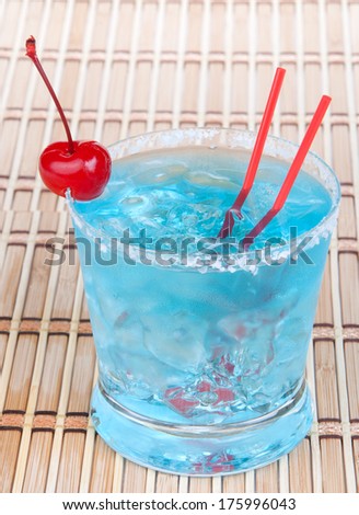 Cocktail blue hawaiian with alcohol, vodka, crushed ice, red cherry and straws on a white background. Focus on cherry