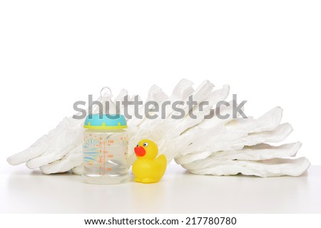 New born child stack of diapers nipple soother baby feeding milk bottle with water and yellow duck on a white background