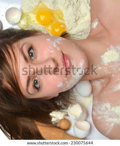 Happy pretty young woman chef with different kitchen tools for cooking and baking sugar eggs wheat looking at the camera on a white background