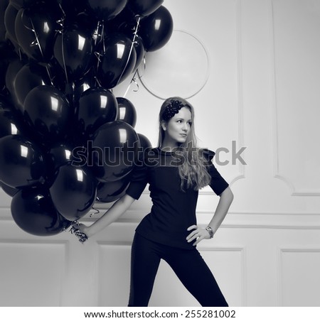 Young happy girl with black balloons as a present for birthday party smiling and looking at the corner black and white picture