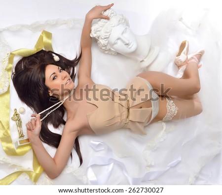 Beautiful alluring young hot woman in sexy lingerie lying on the floor with apollo statue candies pearl necklace in ballets dancer shoes