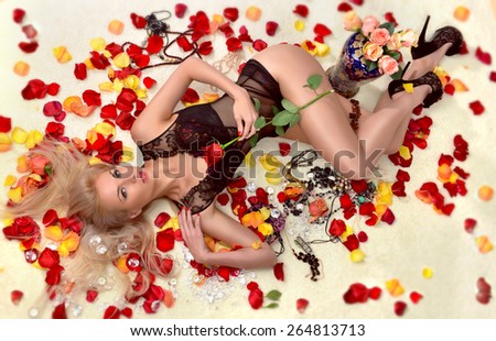 Beautiful young blonde woman lying on floor among red rose petals wearing red sexy bra pants under wear with alluring diamonds jewerly bijouterie