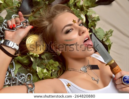 Portrait of beautiful sexy brunette woman with lick sharp hunters knife and chain lying and looking at the camera