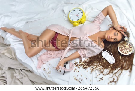 Fashion interior photo of beautiful sexy brunette woman lying in the bed wearing bathrobe in bedroom with morning breakfast food bowl with milk and cereal