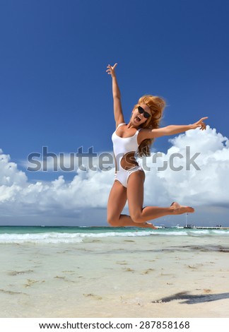 Young sexy woman happy jumping relaxing on tropical beach send with long  windy hair in white bikini and sunglasses