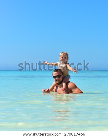 Father and daughter. Dad holding two year old baby girl on neck happy playing smiling in water on sea beach tropical vacation holidays