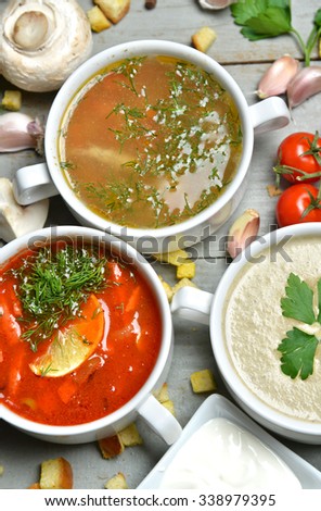 Three different soup bowls composition mushroom cream soup fish and tomato in bowl with garlic parsley dill and croutons on rustic wood background