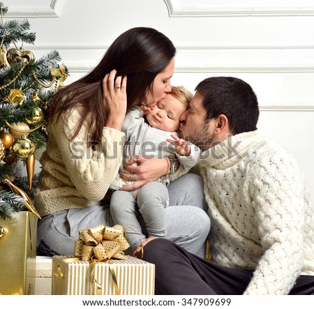 Christmas Family with baby Kid and gold present gifts. Happy kissing Parents and Child at Home Celebrating New Year. Christmas Tree. Christmas scene