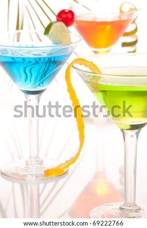 Colorful martini party cocktails with vodka, tequila, juice, lime slice, cherry in martini cocktail glass and tropical palm leaf on a white background