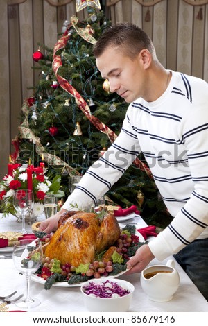 Man with Garnished Thanksgiving roasted turkey to celebrate traditional family dinner with salad, fruits, vegetables, wine and champagne glasses on Christmas tree background