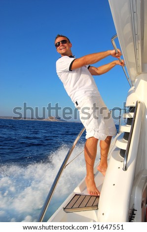 Young Sailor relaxing happily on the vacation sailboat yacht standing on a deck  having a rest on summer boat over blue ocean wave splashes background