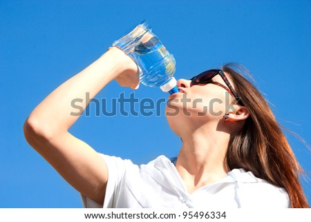 Young woman drinking water on outdoor workout from plastic sports bottle against  blue sky background