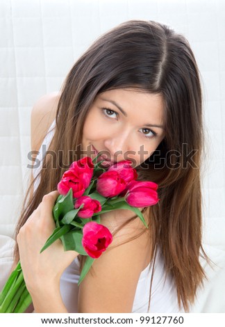 Beautiful young woman with bouquet of red tulips flowers sitting on couch, smiling
