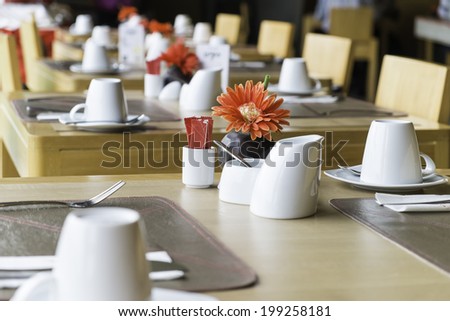 public wood dining table set with white porcelain tableware and decorative objects