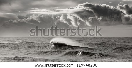Black and white photograph of a wave breaking beneath a storm sky