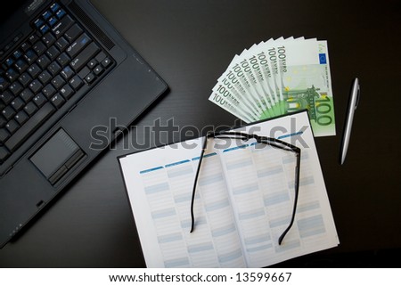Stack of euro on office desktop with organizer and laptop