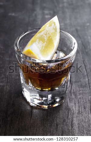 Single glass of tequila with lemon on table