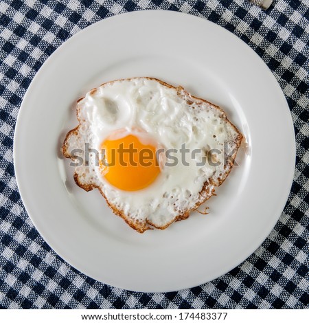 Fried egg in a white plate on checkered tablecloth