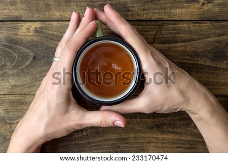 woman hands holding mug of hot drink that standing on wooden table, from above