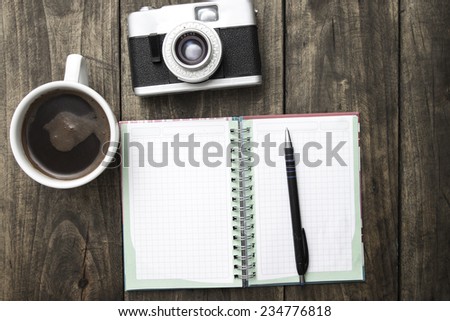 Vintage camera, diary with pan and cup pf coffee on wooden table.