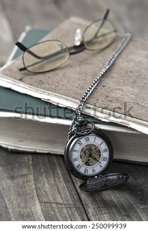 An antique pocket watch, glasses and books in close up