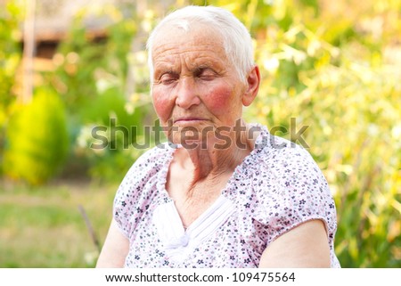 Elderly woman with closed eyes sitting outdoors.