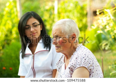Old lady talking to the young nurse / doctor outdoors.