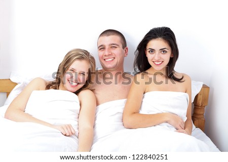 Smiling man in bed between two attractive women- threesome