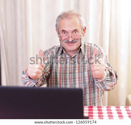 Elderly man with glasses using laptop at home.