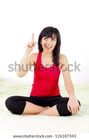 Young woman sitting on bed, pointing upwards having an idea - on white.