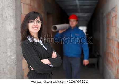 Happy businesswoman / employer smiling to the camera - a construction worker working in the background.