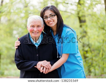 Portrait of caring nurse helping elderly lady holding her hands.