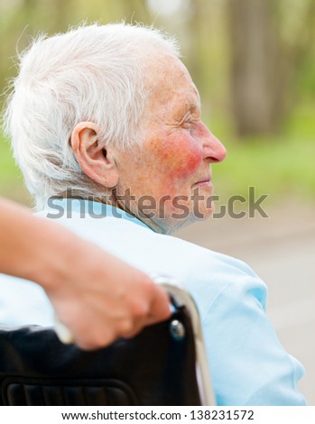 Elderly woman in wheelchair pushed by nurse's hands.