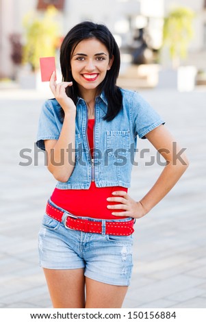 Cute girl with red empty credit card standing in the city center.