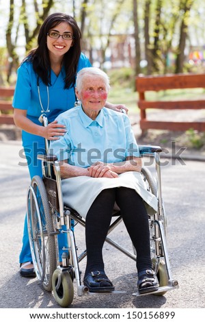 Kind doctor, nurse outdoors taking care of an ill elderly woman in wheelchair.