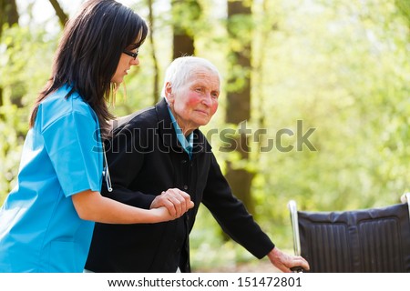 Caring nurse or doctor helping elderly patient to sit down on her wheelchair.