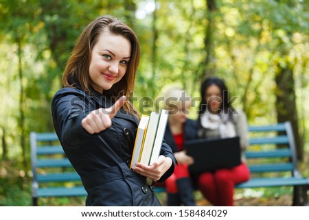 Student showing like sign with books in hand and friends behind.