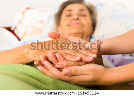 Caring nurse holding kind elderly lady\'s hands in bed.