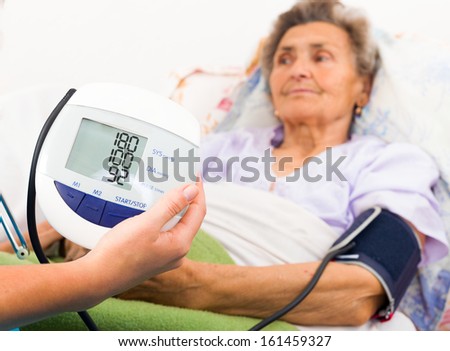 Home care nurse using digital blood pressure measure.