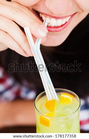 A closeup of a young woman\'s mouth drinking a cocktail with straw.